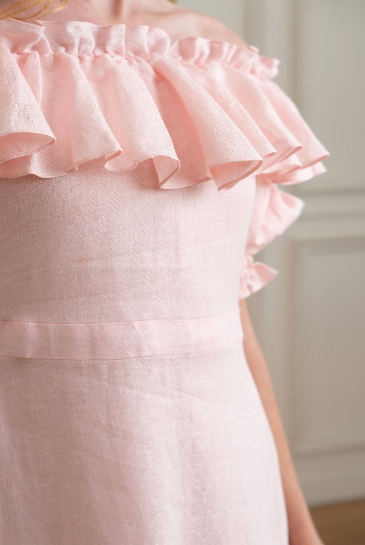 Close-up of a pink dress with ruffled details with self embroidered linen fabric on a neutral background