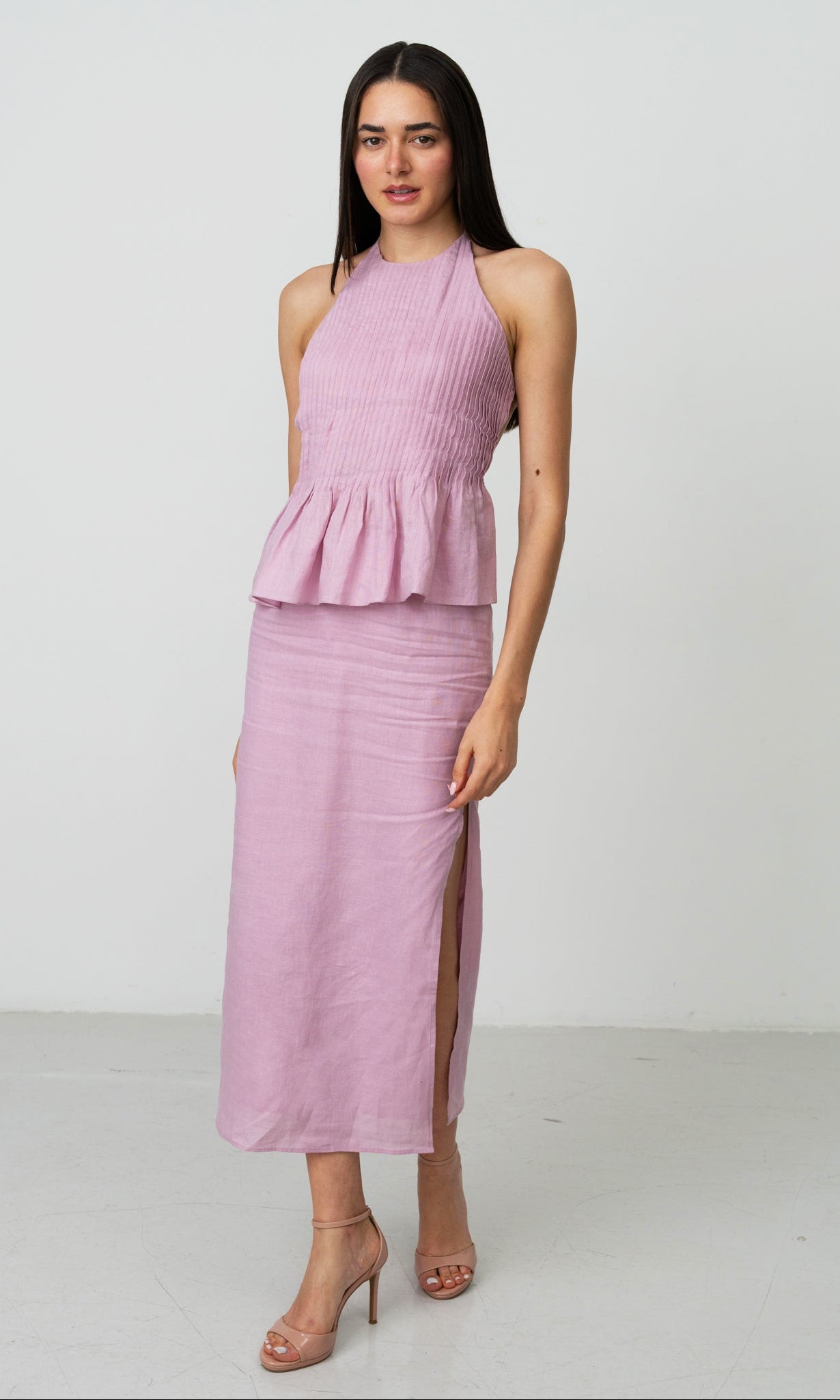 Woman wearing a pink halter dress with a peplum & slits white background