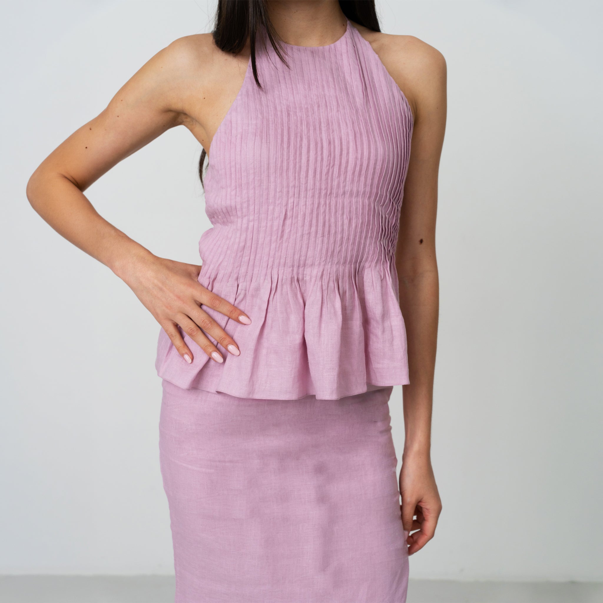 Person wearing a pink halter top and skirt set against a plain background, halter peplum top