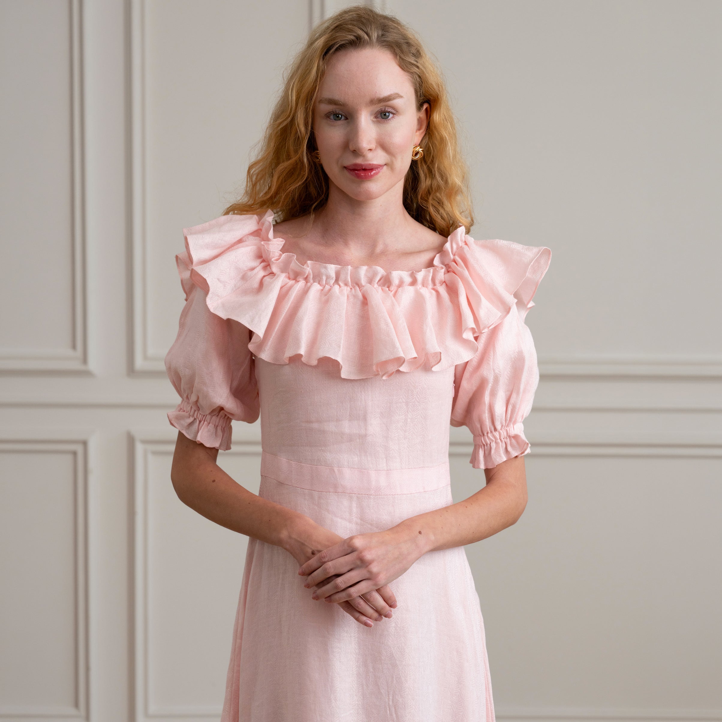 Woman wearing a pink dress with ruffled sleeves against a neutral background