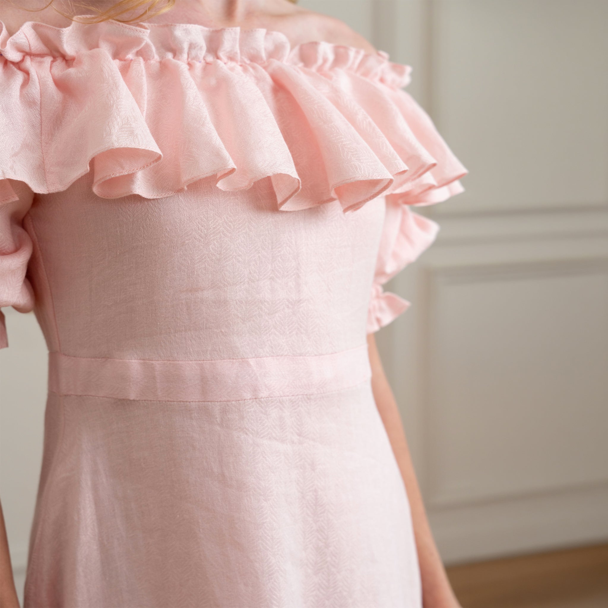 Close-up of a pink dress with ruffled details with self embroidered linen fabric on a neutral background